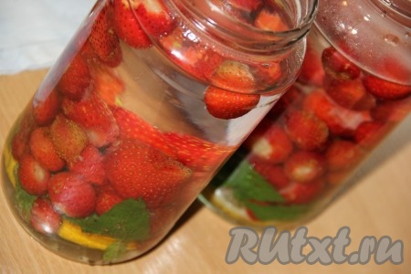 Вскипятить воду и полностью залить банки с клубникой, лимоном и мятой крутым кипятком. Накрыть баночки предварительно прокипячёнными крышками и оставить на 30 минут.
