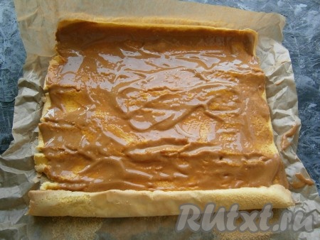 Остывший бисквитный рулет аккуратно развернуть, пергамент снять. Смазать бисквит варёной сгущёнкой, смешанной с маслом и сметаной.
