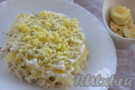 Куриные яйца сварить вкрутую (с момента закипания воды варить минут 10), охладить, очистить, а затем отделить белки от желтков. Белки на время отложить в сторону, желтки натереть на средней тёрке и выложить поверх картошки (майонезом этот слой не смазывать).