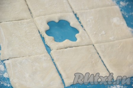 Один пласт слоёного теста будем использовать в качестве донышек слоек, а второй пласт - в качестве верхушек слоек. В квадратах, которые мы будем использовать в качестве верхушек слоек, нужно с помощью формы для печенья вырезать отверстия (я вырезала цветочки).

