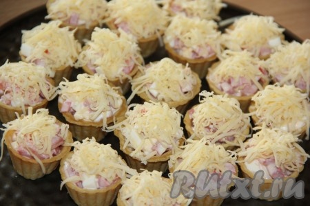 Тарталетки выставить на противень. Сыр натереть на мелкой тёрке и выложить в тарталетки.