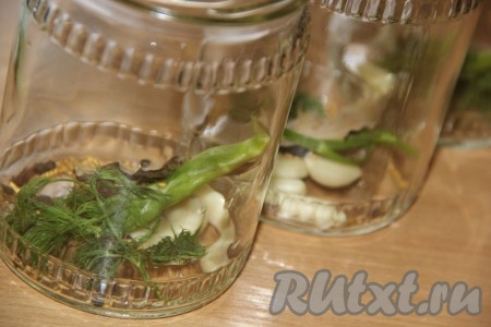 Вымыть и простерилизовать баночки. Выложить на дно каждой банки зонтик (или веточку) укропа, щепотку семян горчицы, лавровый лист. Чеснок очистить, нарезать лепестками (можно оставить зубчики и целыми) и разложить по банкам.
