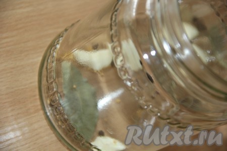 Вымыть и простерилизовать банки любым удобным способом, крышки прокипятить. На дно каждой банки выложить 3 очищенных зубчика чеснока, лавровый лист, 5 горошинок чёрного перца, щепотку семян горчицы.
