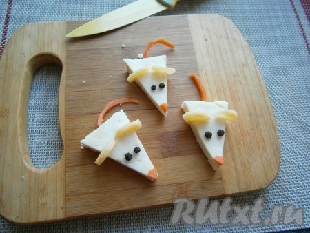 Сделать небольшие разрезы в широкой части треугольников и вставить небольшого диаметра, вырезанные из твёрдого сыра, кружочки (ушки мышей). Вставить глазки из чёрного перца горошком и в конце узкой части разместить кусочки моркови (носики). Хвостики также вырезать из кусочков моркови.

