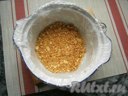 В горячий заварной крем вмешать сливочное масло и дать ему остыть до тёплого состояния. Небольшую форму (диаметр 12-14 см) застелить пищевой плёнкой (и дно, и бока). Насыпать на дно несколько столовых ложек песочной крошки.
