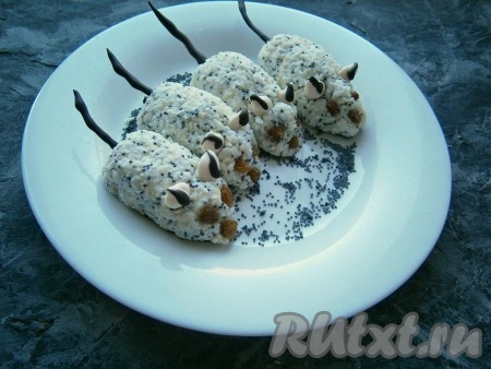 Из творожной массы влажными руками сформировать мышек, разместить их на тарелке, чуть посыпав тарелку маком. Глазки и носик сделать из небольших ягод изюма, ушки - из капель белого шоколада, на который ещё можно нанести полосы из черного шоколада (немного останется в кондитерском мешке) и вставить хвостики из чёрного шоколада. Десерт поместить в холодильник на 30-40 минут.
