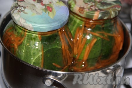 Взять большую кастрюлю, застелить её дно полотенчиком или тряпочкой, сложенной в 2-3 раза (полотенчико или сложенная ткань не дадут банкам лопнуть во время стерилизации), влить тёплую воду. Поставить в кастрюлю банки с огурцами и морковью в маринаде, прикрыв их прокипячёнными крышками, и отправить на средний огонь. Воды в кастрюле должно быть столько, чтобы она покрывала баночки по "плечики". С момента закипания воды в кастрюле стерилизовать банки 20 минут.
