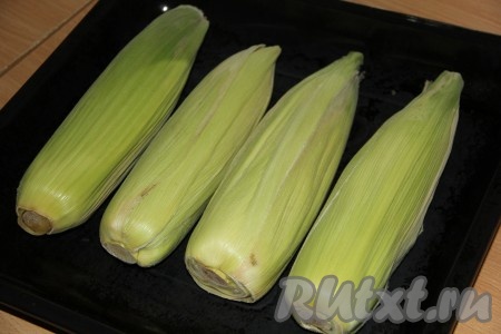 Духовку предварительно разогреть до 180 градусов. Кукурузу выложить на противень для запекания. Листья с кукурузы не удалять! Благодаря листочкам, она сохранит свою сочность в процессе запекания.
