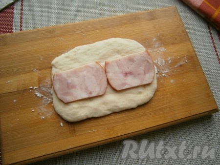 Для формовки каждого пирожка нам из одного кусочка теста нужно раскатать прямоугольник размером около 12х8 см и из скатанного шарика теста лепёшку диаметром около 13-14 см. Итак, на раскатанный прямоугольник теста выложить по середине один (или два) ломтика ветчины на всю длину.
