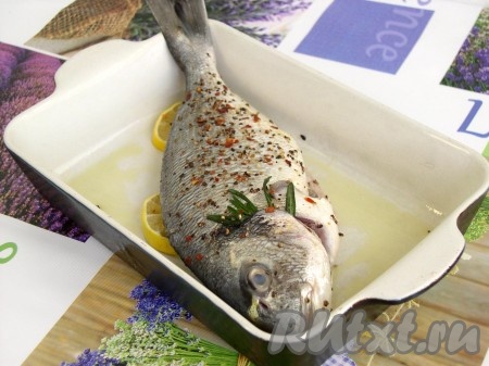 Форму для запекания смазать маслом, выложить кружки лимона. Выложить сверху дорадо, посыпать специями (это больше для декора). Внутрь брюшка вложить веточку розмарина, можно также и лимончика дольку. При запекании свежий розмарин даёт тонкий аромат, который оригинально подчёркивает достоинства этой рыбы (если розмарин - не ваша специя, можете использовать лимонный перец).
