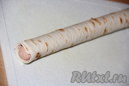 Плотно завернуть сосиски в лаваш в три оборота.