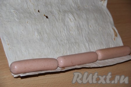 Сосиски очистить от слюды. На край лаваша выложить сосиски.
