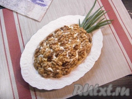 Поверх салата выложить половинки (или четвертинки) ядер грецких орехов, сбоку выложить перья зелёного лука (как на фото), придавая салату вид ананаса.
