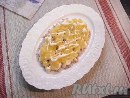 Нарезать ананасы мелкими кусочками и выложить на куриное мясо вторым слоем, смазать немного майонезом.
