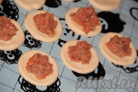 На столе, припылённом мукой, раскатать тесто в тонкий пласт и вырезать кружочки с помощью стакана. На серединку каждого кружка из теста выложить немного рыбного фарша.
