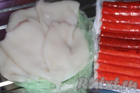 Разморозить тушки кальмаров и крабовые палочки при комнатной температуре. Если вы приобрели неочищенных кальмаров, тогда удалите с поверхности тушек тёмную плёнку, уберите хорду. Затем очищенных кальмаров нужно промыть водой.
