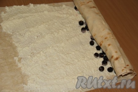 Не подворачивая края и начиная с края с творогом и ягодами, свернуть лаваш в тугой рулет. 
