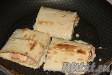 Влить в сковороду растительное масло, разогреть, выложить рулетики из лаваша с начинкой из колбасы, сыра и помидоров.
