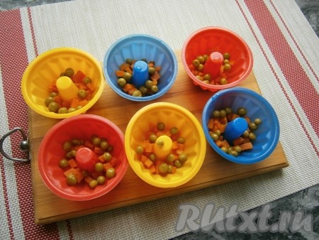 В формочки для кексов выложить немного нарезанной кубиками варёной морковки и по 1 чайной ложке зелёного консервированного горошка (если нет горошка, то можете обойтись и без него).
