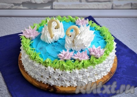 Дальше с помощью насадки "звёздочка" отсадить  из белого крема небольшие цветочки из кулинарного мешка, украсив бока торта. Лебедей можно сделать той же насадкой - вначале выдавив побольше крема в виде полосы (туловище) и также, по бокам, полосы потоньше (крылья), а затем резкими движениями вверх выдавливать крем в виде перьев. Нужно сделать так, чтобы вид лебедя был воздушным. Вставить аккуратно шеи из застывшего шоколада, предварительно окрасив клюв красным красителем и нарисовать глазки в виде точек из чёрного шоколада. Стык верха и боков торта покрыть травой, окрасив часть белого крема зелёным красителем, используя насадку "травка". Цветы сделать с помощью насадки "мелкая хризантема", окрасив белый крем в пурпурный краситель. Необычайно вкусный, нежный, красивый торт "Лебединое озеро" отправить в холодильник на 5-6 часов и можно удивлять родных и гостей.