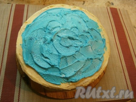 Достать торт и смазать его сверху с помощью ложки (или узкой лопатки) голубым кремом, сделав как бы волны. Должен получиться вид озера или реки. Посыпать сверху пищевыми блёстками.
