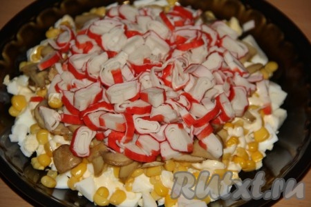 Затем выложить слой из жареных шампиньонов. Крабовые палочки разморозить при комнатной температуре и очистить от слюды. Нарезать крабовые палочки на кружочки и выложить следующим слоем.