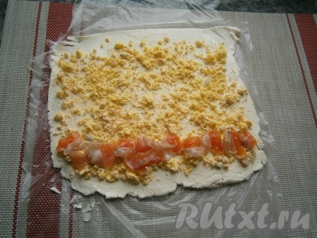 Яйца предварительно отварить вкрутую (варить минут 10 от начала кипения воды), остудить и очистить, разделить на белки и желтки. Посыпать пласт плавленного сыра натёртыми желтками, на нижний край выложить в ряд (горизонтально) кусочки слабосолёной сёмги.
