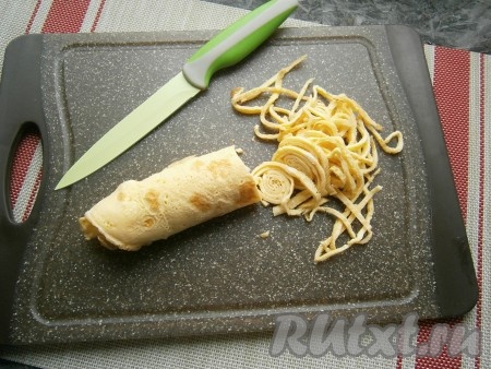 Сложить остывшие яичные блинчики друг на друга, свернуть в плотный рулет и нарезать тонкой лапшой.
