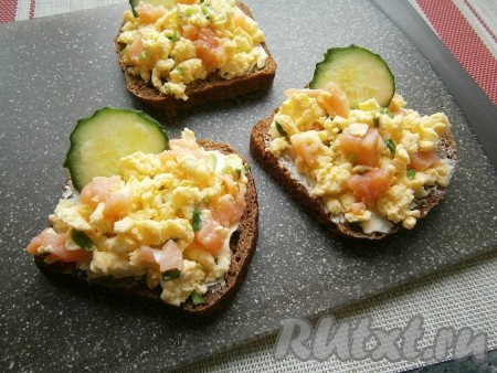 Ломти чёрного хлеба смазать оставшимся размягчённым сливочным маслом и сверху выложить омлет. Украсить бутерброды кружочками свежего огурца.
