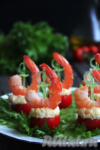 Наполнить помидоры черри начинкой из креветок и яиц. По одной креветки, из тех, что мы оставляли для украшения, выложить поверх каждого фаршированного помидора и зафиксировать шпажкой для канапе. Переложить помидоры черри, фаршированные креветками, на тарелку с листьями салата и подать к столу. Закуска получается очень яркой, красивой и, конечно, вкусной, она точно не останется незамеченной на праздничном столе!
