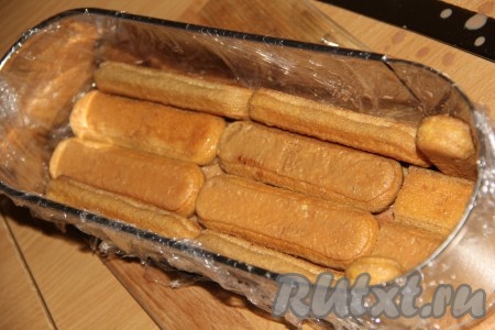 Форму (у меня продолговатая форма размером 28х15 см) застелить пищевой плёнкой. Обмакнуть печенье "Дамские пальчики" в смесь молока и какао и выложить в форму в один слой.
