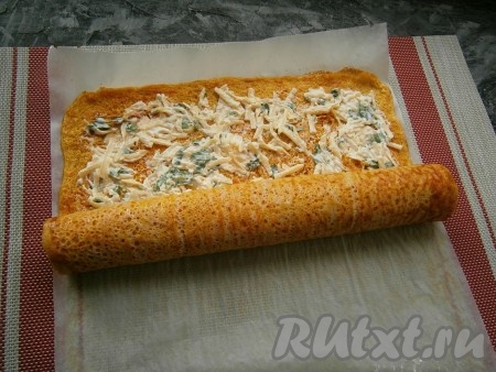 Помогая себе пергаментом,  морковный корж свернуть в плотный рулет, начиная с узкой стороны.