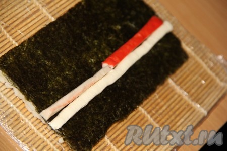 Затем лист нори нужно перевернуть так, чтобы рис оказался внизу. Отступив немного от края нори, ближе к стороне, на которую не выкладывали рис, выложить полоску творожного сыра (для того чтобы полоска сыра была ровной, я выкладываю сыр в кулинарный мешок, а затем выдавливаю его на нори) и брусочки крабовых палочек (как на фото).
