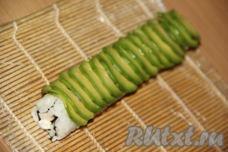 Авокадо разрезать на две части и удалить косточку. Очистить авокадо от кожуры и тонко нарезать мякоть. Выложить кусочки авокадо внахлёст поверх риса.
