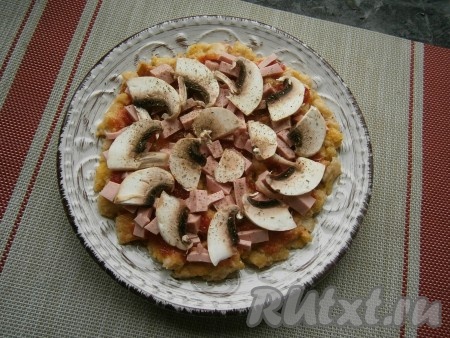 Сверху выложить нарезанную кусочками варёную колбасу и нарезанные тонкими пластинами свежие шампиньоны, немного посолить и посыпать травами.
