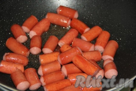 В сковороду влить растительное масло, разогреть на огне, затем выложить сосиски и обжарить их на сильном огне, примерно, 3 минуты, периодически переворачивая. Сосиски должны подрумяниться со всех сторон.
