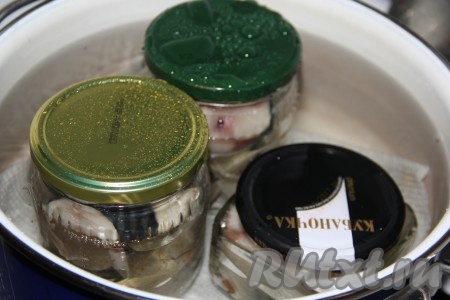 На дно кастрюли выложить хлопчатобумажное полотенце. В кастрюлю на полотенце поставить банки, влить воду по плечики баночек. Кастрюлю с банками с рыбой поставить на средний огонь.
