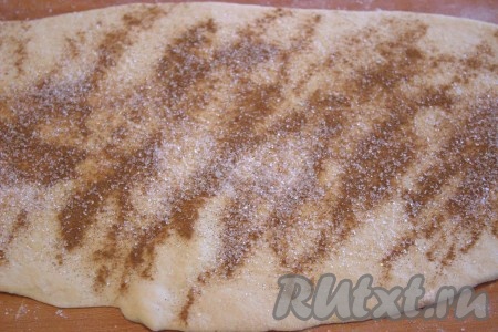 Затем подошедшее тесто разделить на две части. Рабочую поверхность припылить мукой, раскатать одну часть теста в прямоугольник размером 18 сантиметров на 25 сантиметров, затем равномерно присыпать половиной от общего количества молотой корицы и сахара, необходимых для начинки.