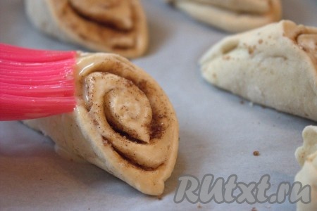 Противень выстелить пергаментной бумагой (или смазать растительным маслом), выложить подготовленные булочки с сахаром и корицей, накрыть полотенцем и дать подняться в течение 30 минут. По прошествии времени, для того чтобы выпечка получилась с румяной корочкой, смазать подошедшие дрожжевые булочки яйцом, взбитым с молоком.
