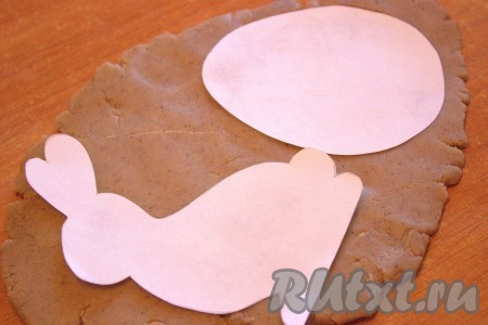 Достать из холодильника охлаждённое тесто и разделить на несколько частей. Одну часть теста раскатать в пласт толщиной, примерно, 3-5 миллиметра. Остальное тесто оставить в холодильнике. При помощи формы или выемки для пряников (или печенья) вырезать нужные нам фигурки. Я распечатала картинки на принтере, вырезала трафарет из бумаги, затем приложила трафарет к раскатанному тесту и вырезала ножом пряники, обводя по контуру. Остатки теста вновь скатать в шар, достать ещё часть теста из холодильника и повторить процедуру. Я сделала заготовки пряников в форме пасхальных кроликов, пасхальных яиц и куличей.
