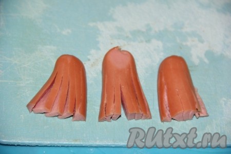 Каждую сосиску разрезать в длину на 2 части (я использовала "детские" сосиски, они чуть меньше обычных сосисок). Затем каждую половинку разрезать по горизонтали на две части (то есть каждая сосиска будет разрезана на 4 части). Каждую получившуюся часть сосиски разрезать, не дорезая до конца, на тонкие полосочки (как на фото) - у нас как бы получатся ножки осьминога.
