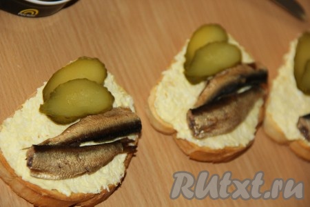 Солёный огурец нарезать тонкими ломтиками. Выложить по два кусочка солёного огурчика на бутерброд рядом со шпротами.
