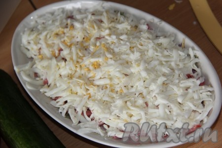 Яйца предварительно сварить вкрутую (в течение 10 минут с начала кипения). Разделить остывшие и очищенные яйца на желтки и белки. 2 желтка оставляем для украшения, белки нужно натереть на крупной тёрке. Выложить белки поверх колбасы.
