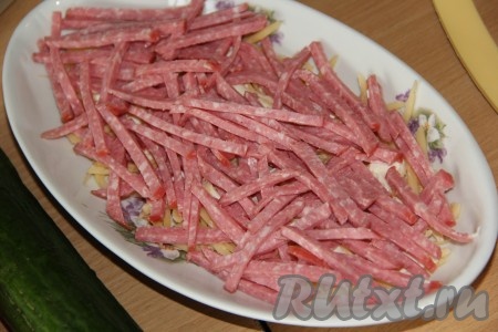 Колбасу нарезать длинными брусочками. Часть колбасы оставляем для украшения. Выложить колбасу поверх сыра.
