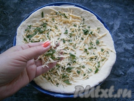 Немного обмять тесто смазанными растительным маслом руками. Для удобства разделить тесто на 2 части и каждую из частей раскатать в лепёшку толщиной, примерно, 0,5 см на подпылённом мукой столе. Посыпать каждую лепёшку половиной от общего количества сыра с зеленью.
