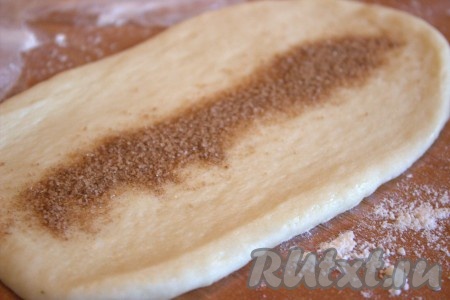 Каждый шарик теста раскатать в овал шириной, примерно, 6-7 сантиметров и длиной, примерно, 10 сантиметров. Для приготовления начинки соединить сахар и корицу, тщательно перемешать. На середину раскатанного теста выложить часть начинки из сахара и корицы.
