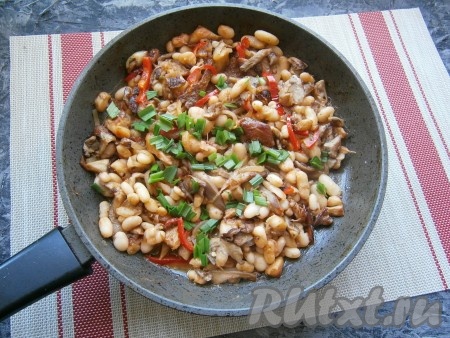 Всыпать сахар, влить воду, перемешать, добавить измельчённую зелень чеснока. Тушить фасоль с грибами в томатном соусе на небольшом огне, периодически помешивая, 4-5 минут.

