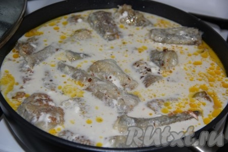 Влить сметанный соус в сковороду к рыбе с овощами, дать закипеть. Затем тушить минтая под крышкой на медленном огне с момента закипания в течение 10-15 минут.