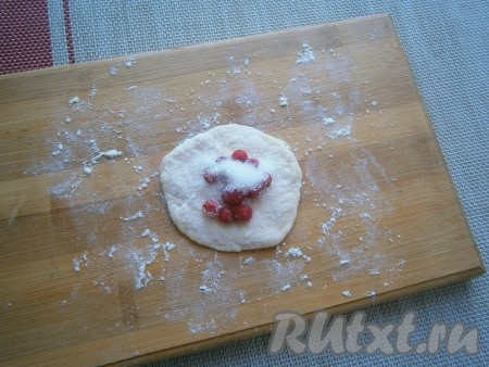 На припылённой мукой поверхности каждый кусочек теста размять в лепёшку. В середину каждой лепёшки выложить по 10-12 ягодок красной смородины, сверху присыпать ягоды 0,5-1 чайной ложкой сахара.
