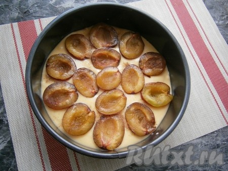 Дно разъёмной формы диаметром 22-24 см застелить пергаментной бумагой, выложить половину теста. На тесто, срезом вверх, разложить сливы в один слой, посыпать их молотой корицей.